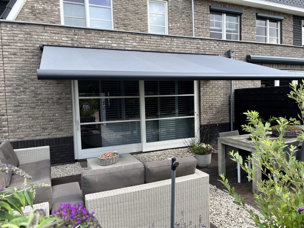 Buitenzonwering knikarm zonnescherm in de achtertuin van een huis.